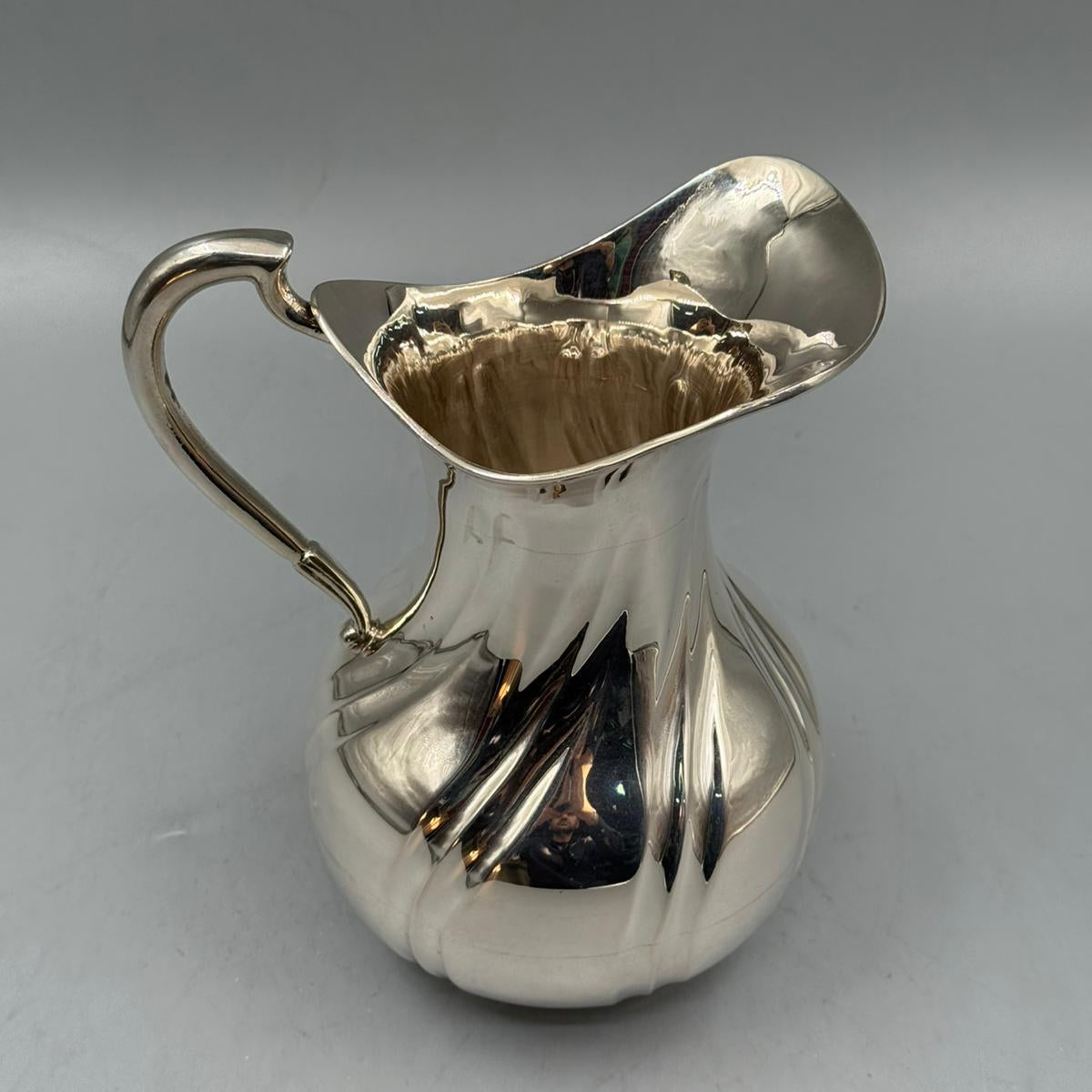 A reflective silver pitcher with a sculpted body, tall neck, and gracefully curved spout.