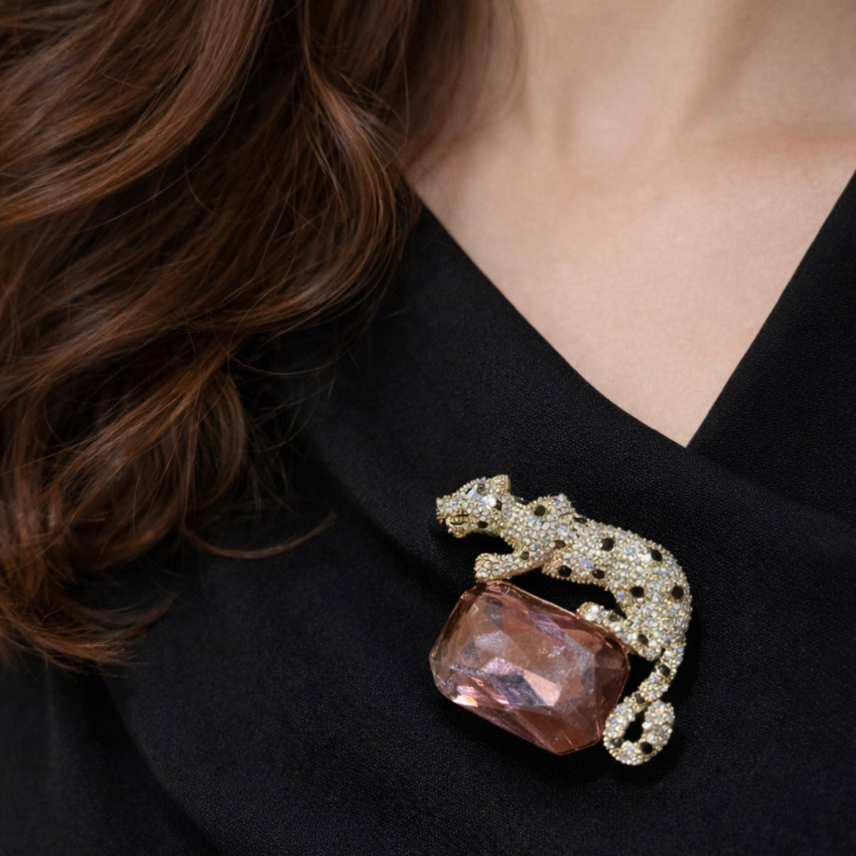 A statement gold-plated panther brooch fully encrusted with clear and black pave crystals, resting elegantly on a large, rectangular faceted pink gemstone.
