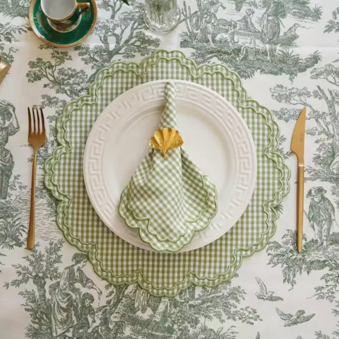 Corner detail of a green toile tablecloth showing the print placement, clean hem, and fabric texture.