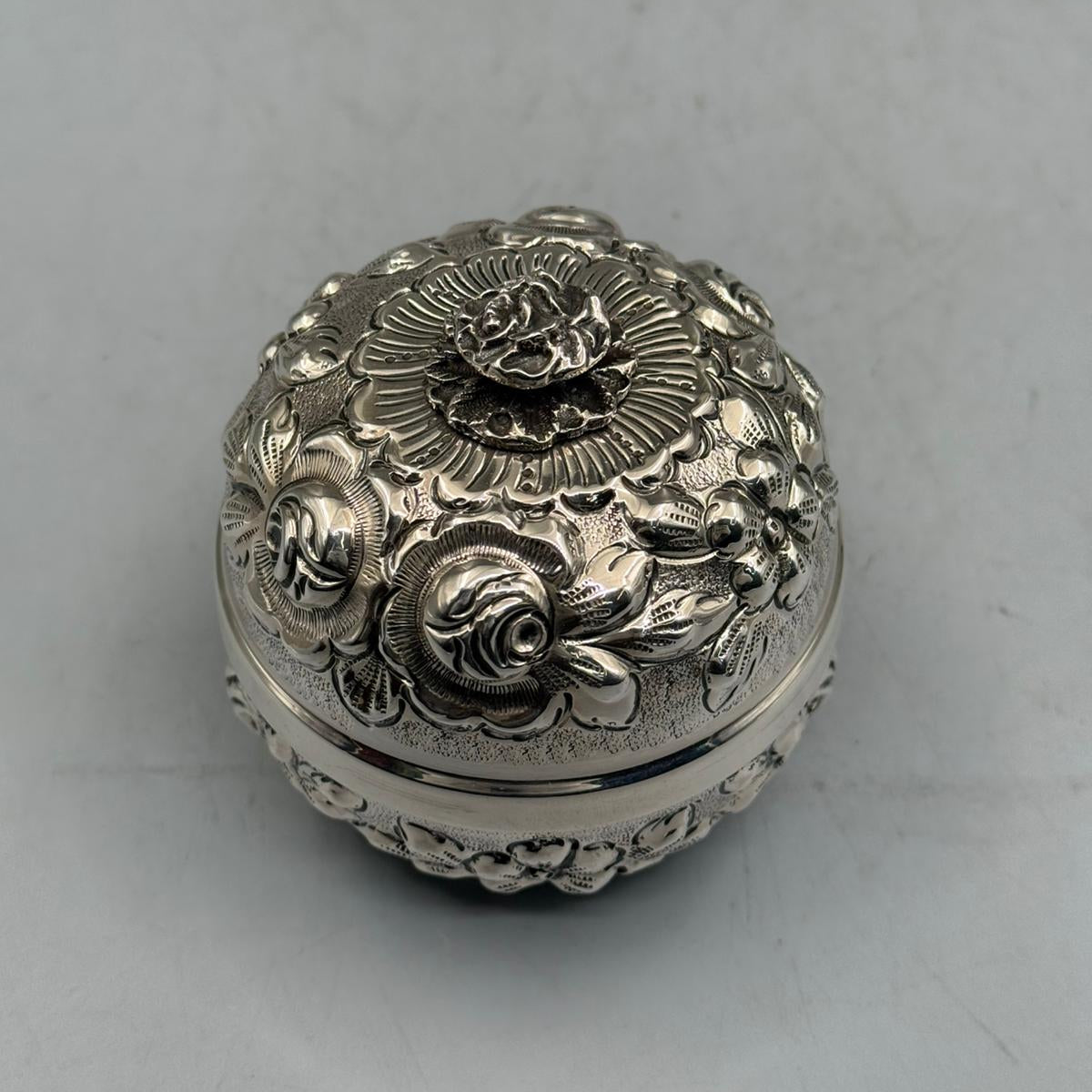 Top-down perspective of the sculpted silver rose handle and the radial embossed floral patterns on the sterling silver lid.