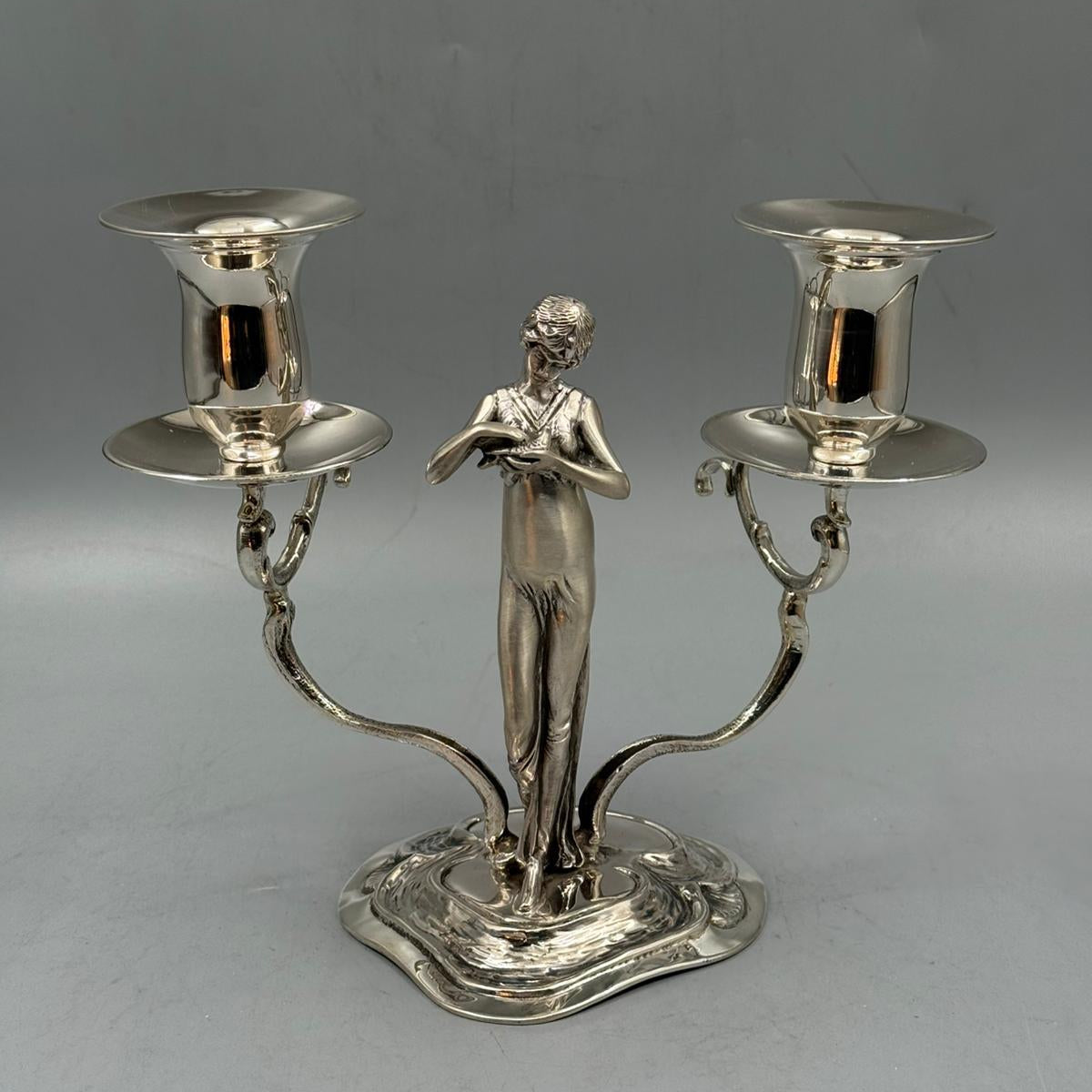 Side view of a silver candlestick featuring a woman design and two candle holders.