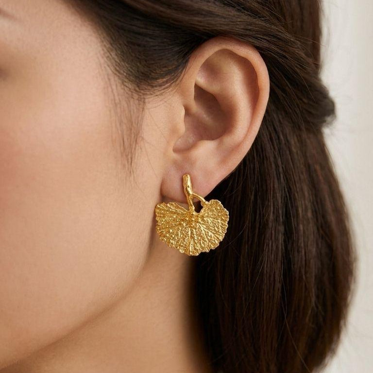 Close-up view of organic Ginkgo biloba leaf stud earrings, a unique botanical jewelry design. These gold plated silver statement earrings showcase intricate leaf veining and a refined matte-like finish.