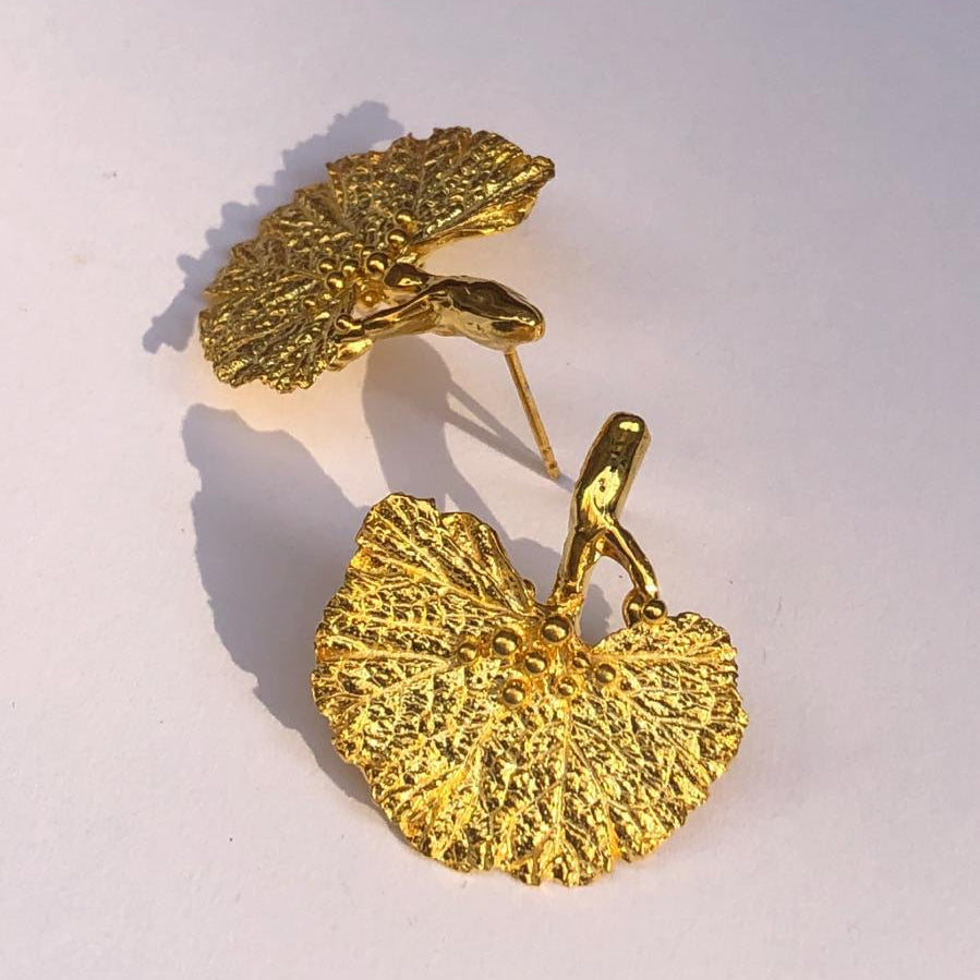 A pair of handcrafted 18K gold-plated 925 sterling silver stud earrings. Each earring features a detailed casting of a real fanned Ginkgo biloba leaf with its sapling stem. The earrings have a stunning organic texture, measuring 2.5 cm by 2.5 cm.