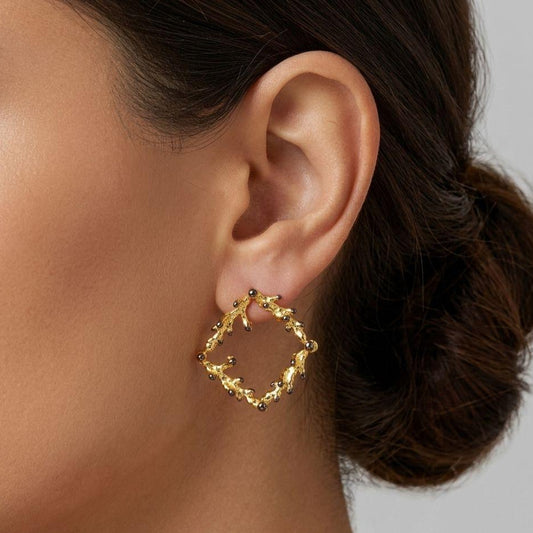 A pair of handcrafted 925 sterling silver stud earrings forming a square frame. The organic pine branch design is 18K gold-plated, beautifully contrasted with dark oxidized tips on the natural buds. Measuring 3 cm by 3 cm.