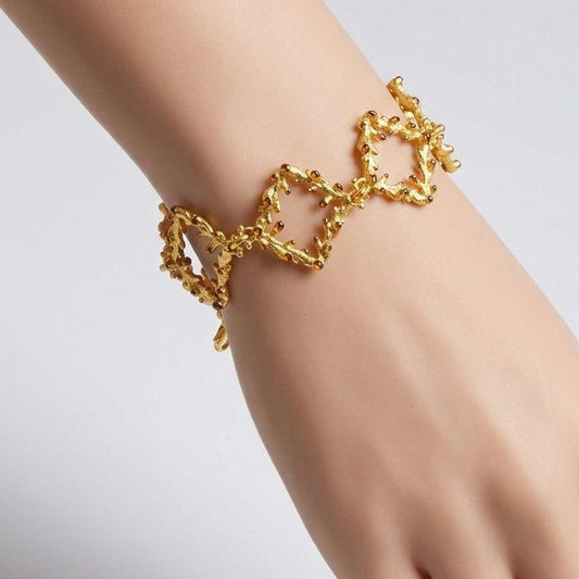A handcrafted statement bracelet made of interlocking 925 sterling silver square links. The organic pine branch design is 18K gold-plated with dark oxidized tips, measuring 18 cm long.