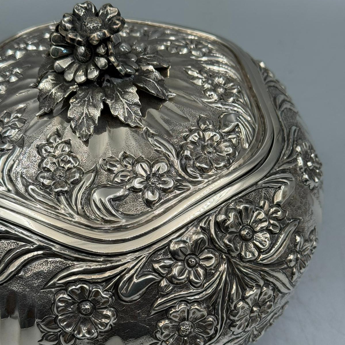 Close-up of the 3D flower handle and deep-relief floral engravings on the handcrafted 900 sterling silver lid.