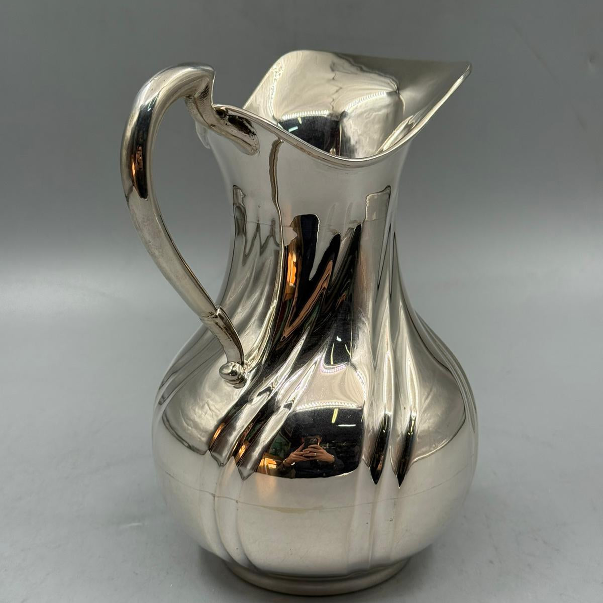 A polished silver jug showcasing a rounded form, smooth surface, and flared spout opening.