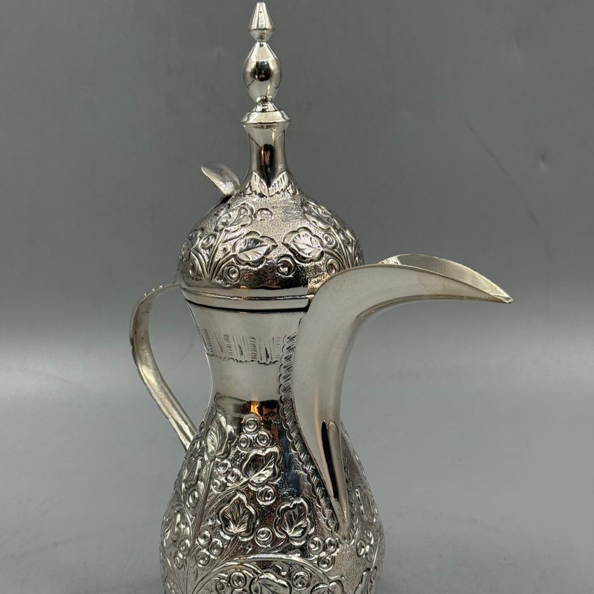 A polished silver Arabic-style coffee pot featuring floral engravings and a pointed finial on the lid.