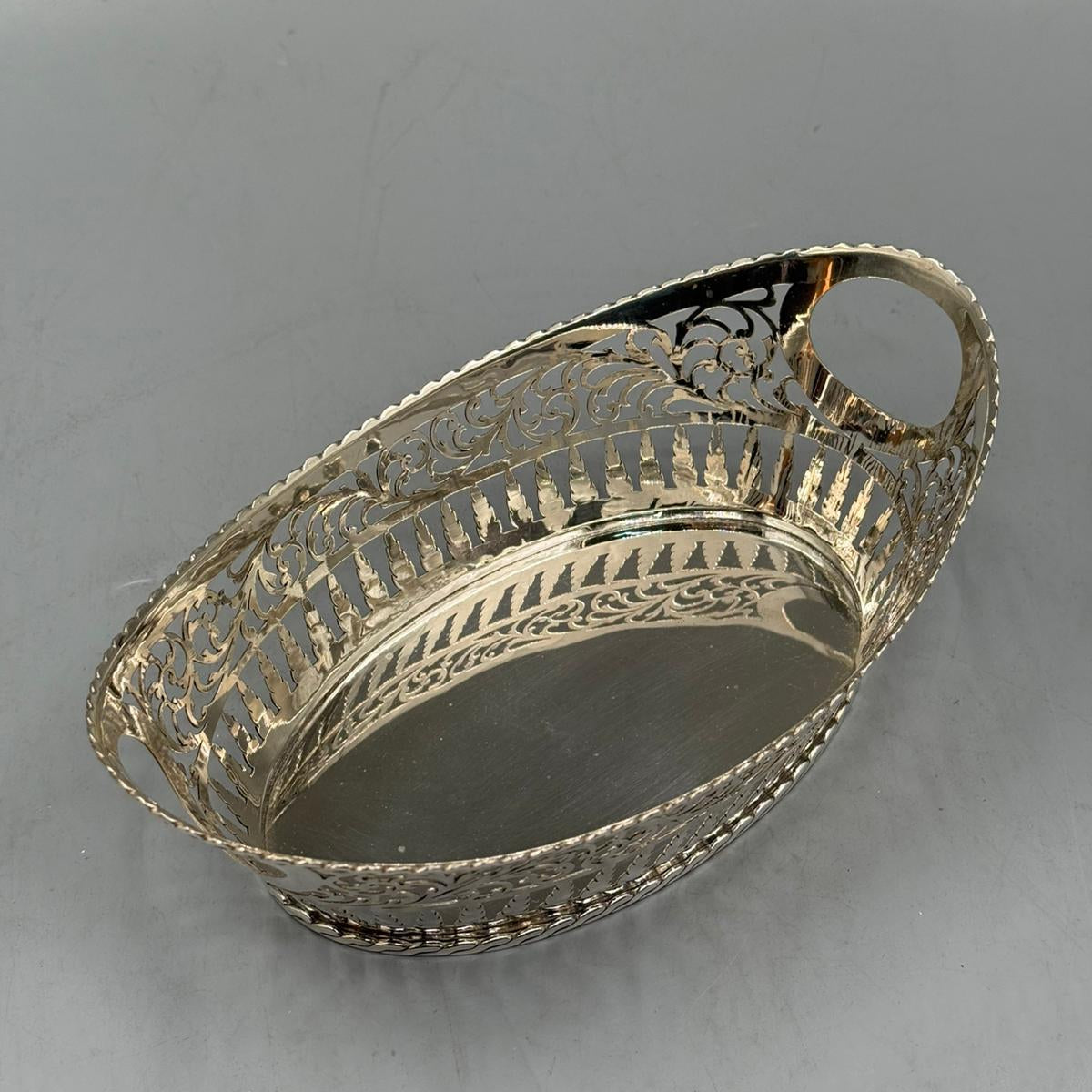 An oval silver tray with decorative pierced floral patterns and two side handles, perfect for serving or display.