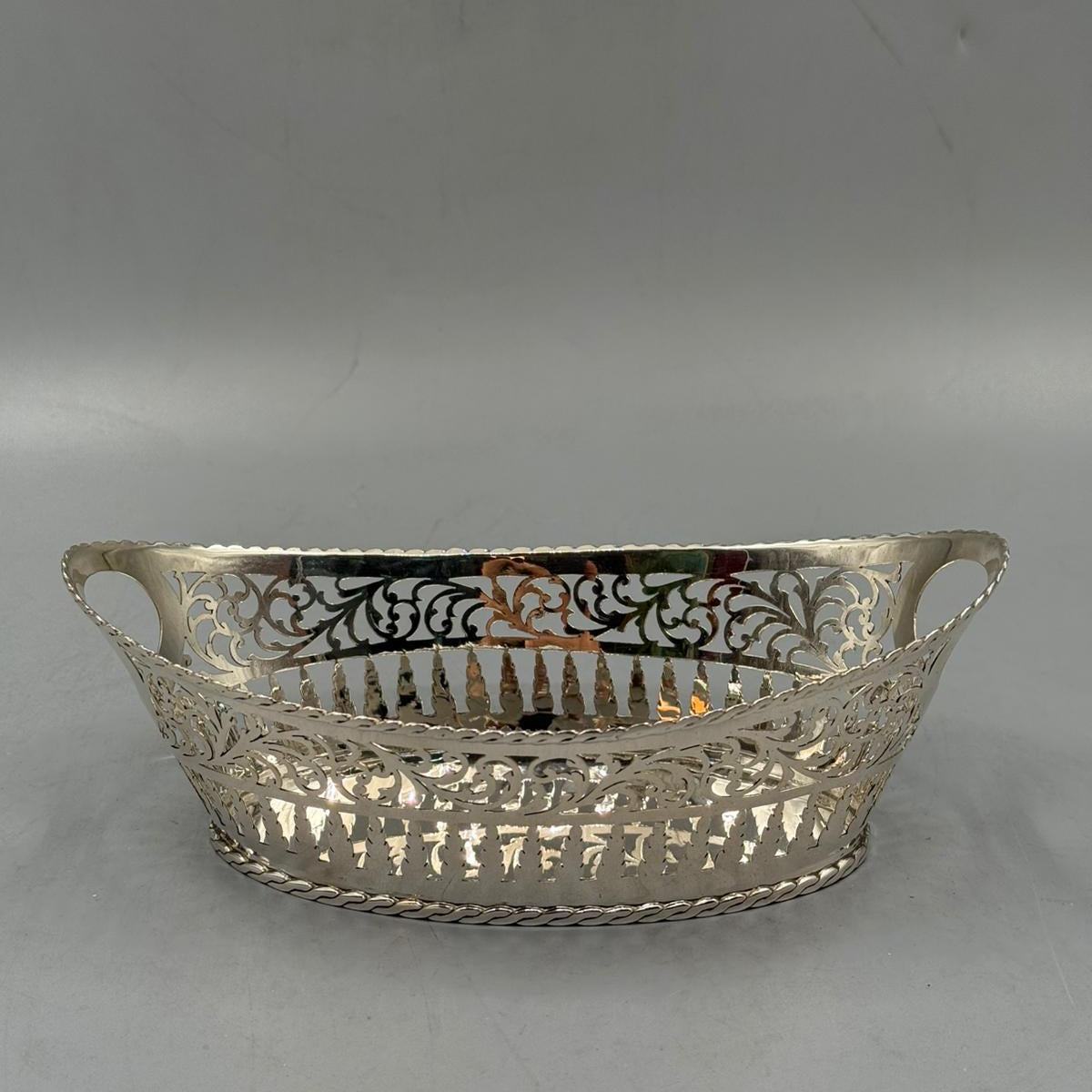 An antique silver serving tray in oval shape, featuring intricate cut-out floral patterns and a round side handle.