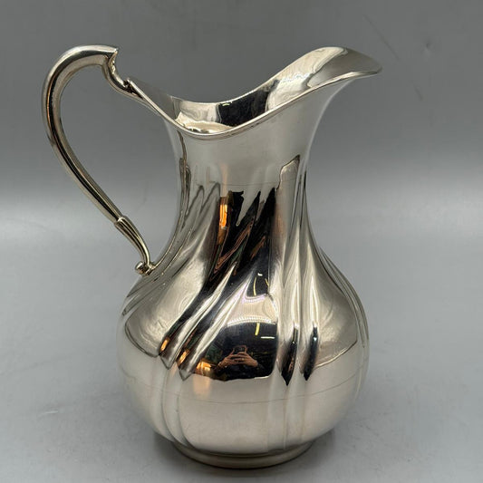 A shiny silver jug featuring a bulbous base, curved handle, and a wide square-shaped spout.