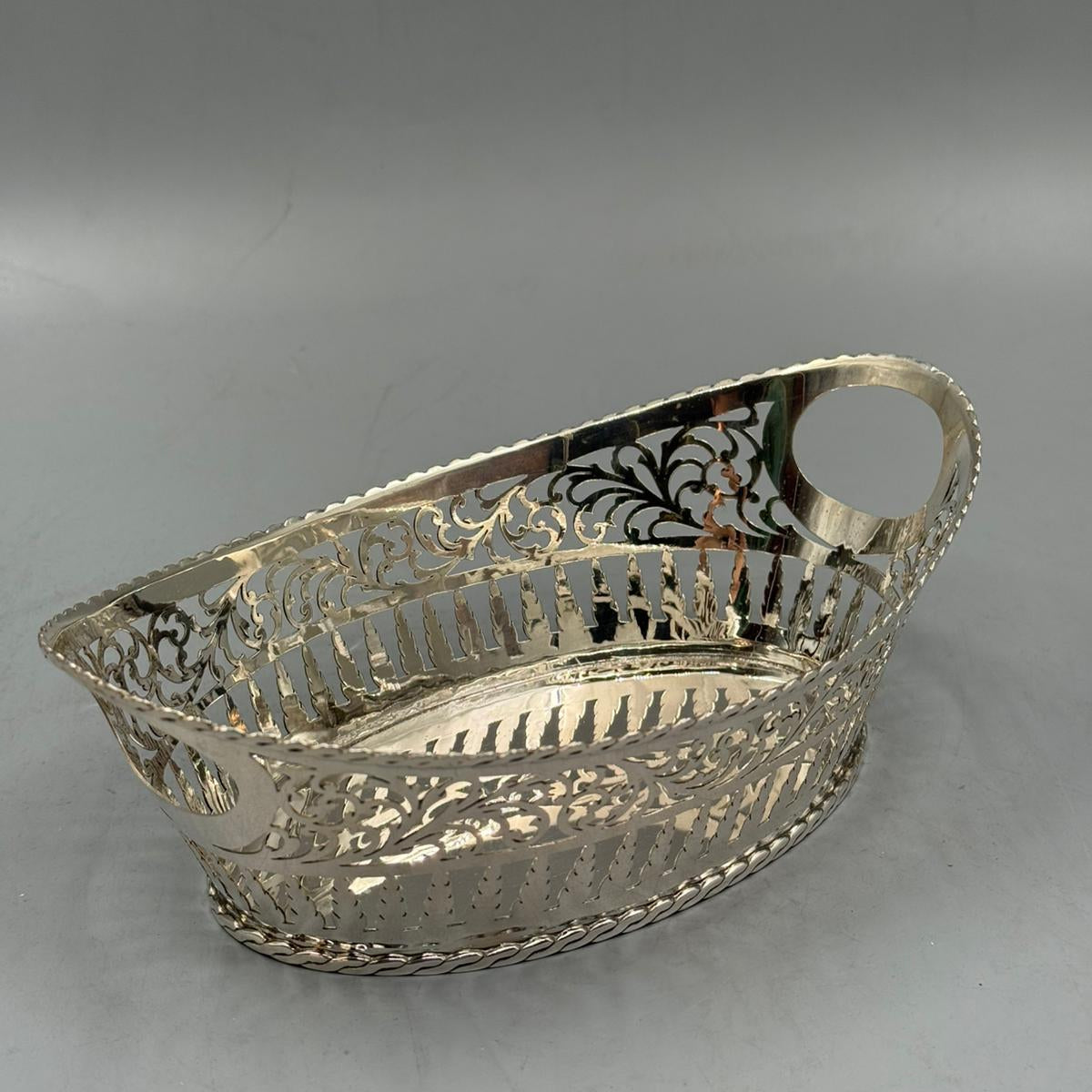 A polished silver oval basket with detailed pierced patterns, raised edges, and elegant handles.