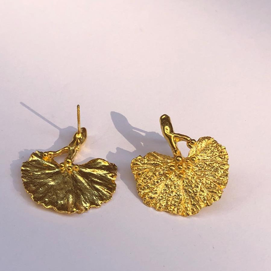 A pair of handcrafted 18K gold-plated 925 sterling silver stud earrings. Each earring features a detailed casting of a real fanned Ginkgo biloba leaf with its sapling stem. The earrings have a stunning organic texture