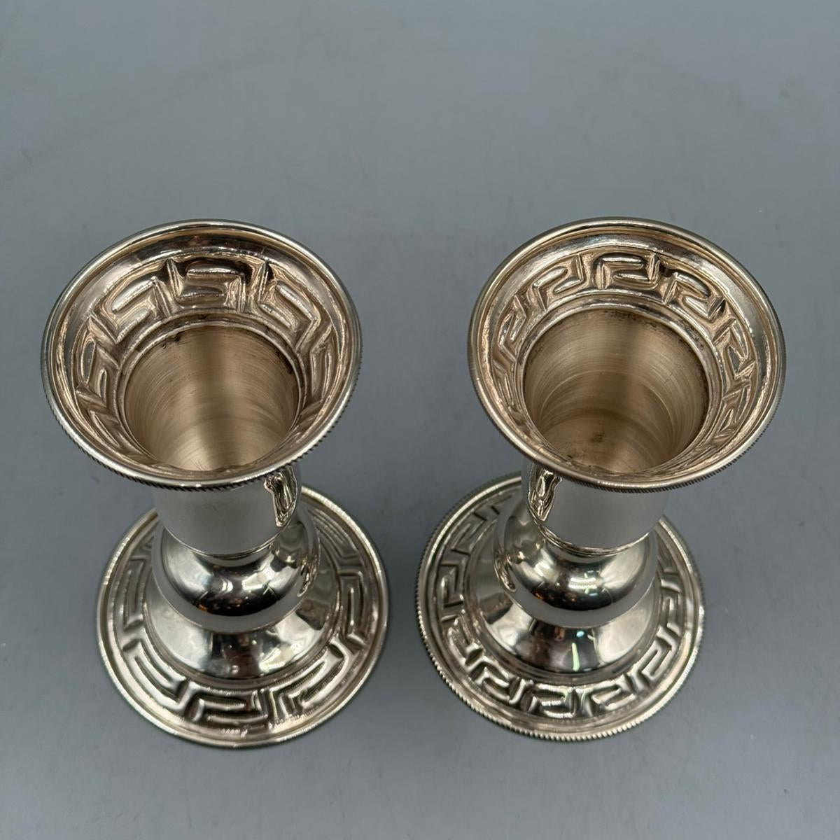 Front view of two antique silver candle holders with ornate Greek key border.