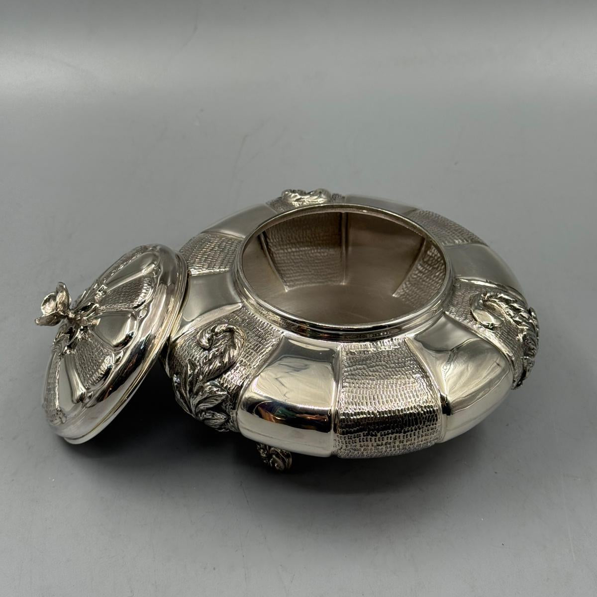 Antique silver round box with decorative legs and a textured surface