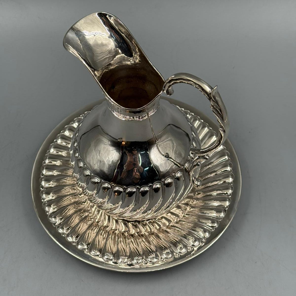Antique silver water pitcher with ornate handle placed on matching silver plate