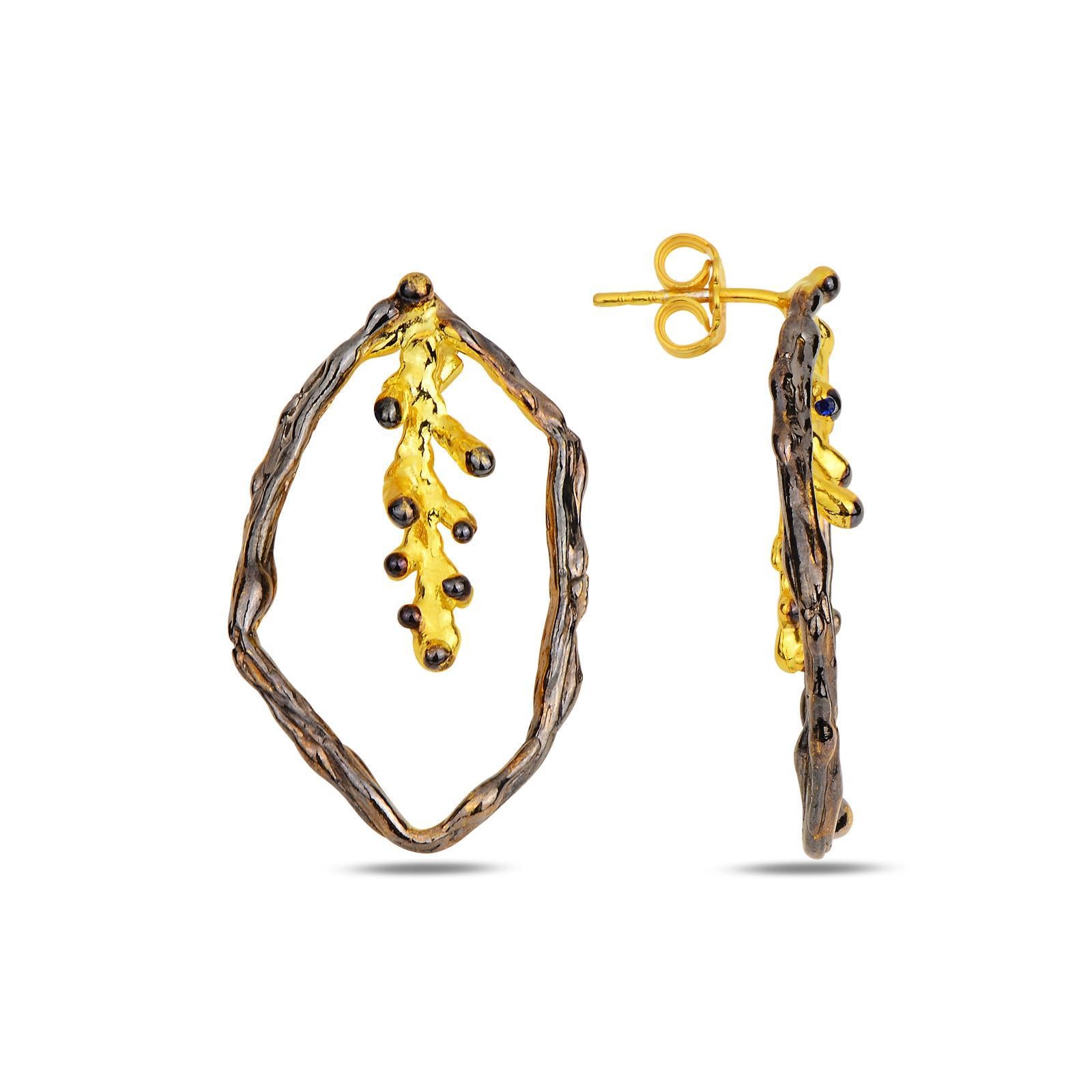 Detailed view of the organic hoop shape and the delicate dangling pine twig within the statement earrings, highlighting the premium craftsmanship and botanical textures.