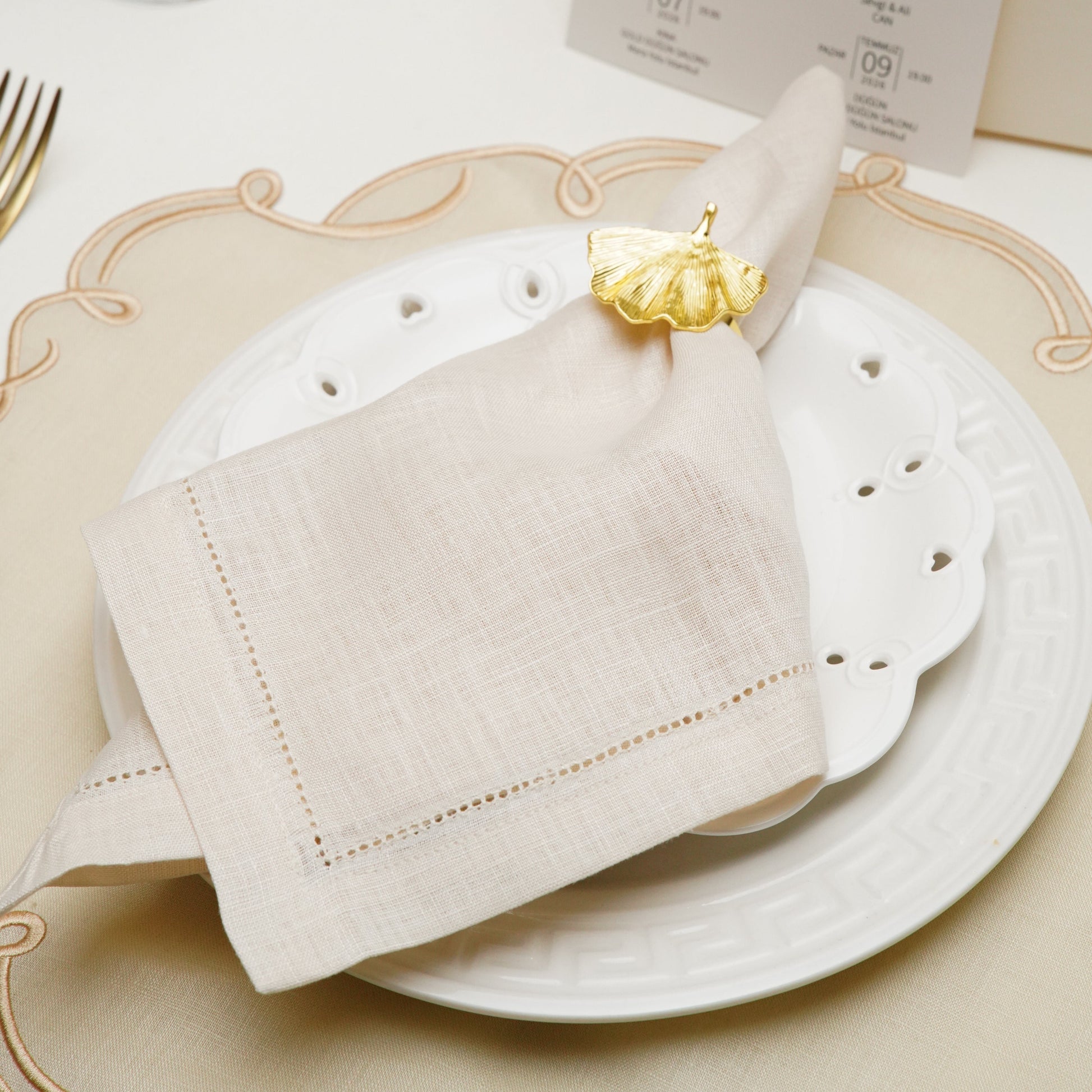 A clean product photograph of a bespoke white linen cloth napkin with custom navy blue embroidery, showing the intricate detail of the initial W and its surrounding crest.