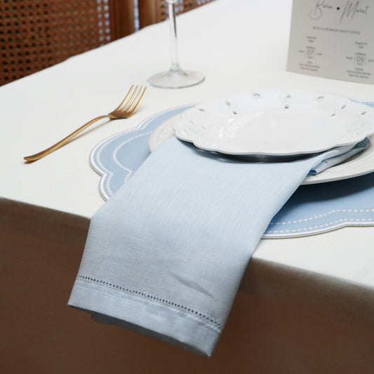 Close-up of a white cloth napkin featuring an intricate embroidered crest monogram in gold and pastel thread, placed on a rich navy velvet tablecloth with gold cutlery and crystalware.