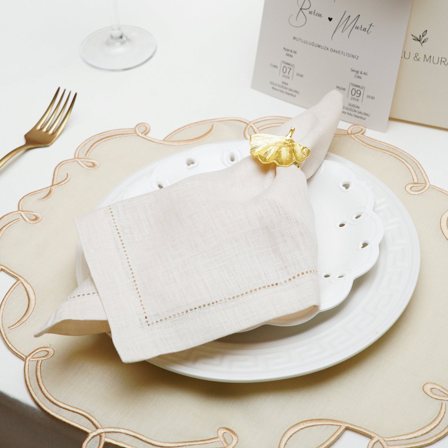 A close-up view of a premium white cloth napkin featuring a custom navy blue embroidered crest and a stylized initial W, suitable for elegant wedding table settings.