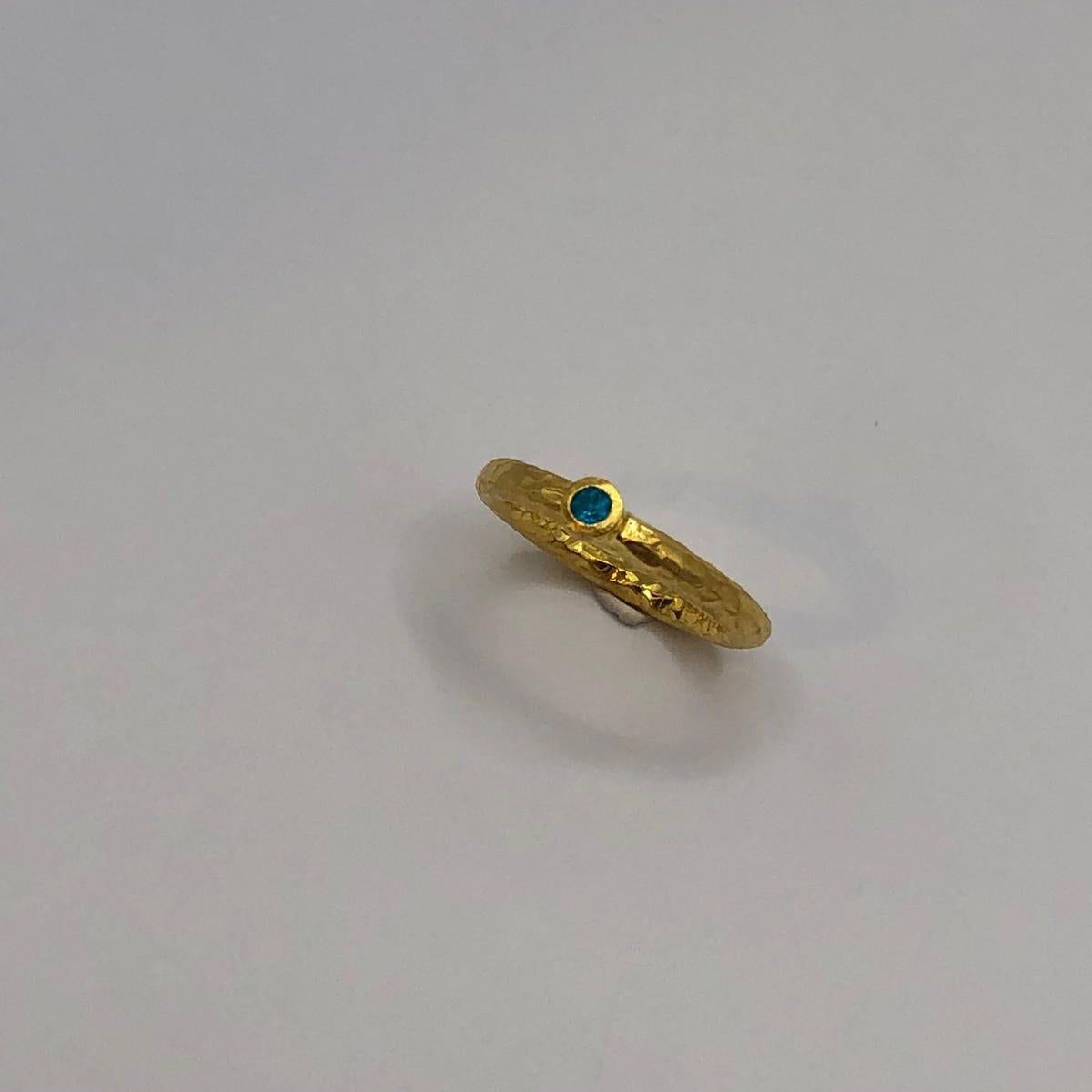 Close-up view of the dainty textured gold ring, highlighting the intricate organic surface and the beautiful pop of blue color from the natural blue topaz gemstone.
