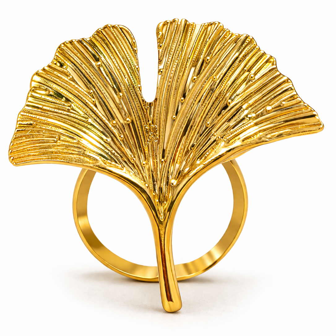 A close-up studio shot of an elegant gold metal napkin ring shaped like a detailed ginkgo leaf, set against a clean white background.