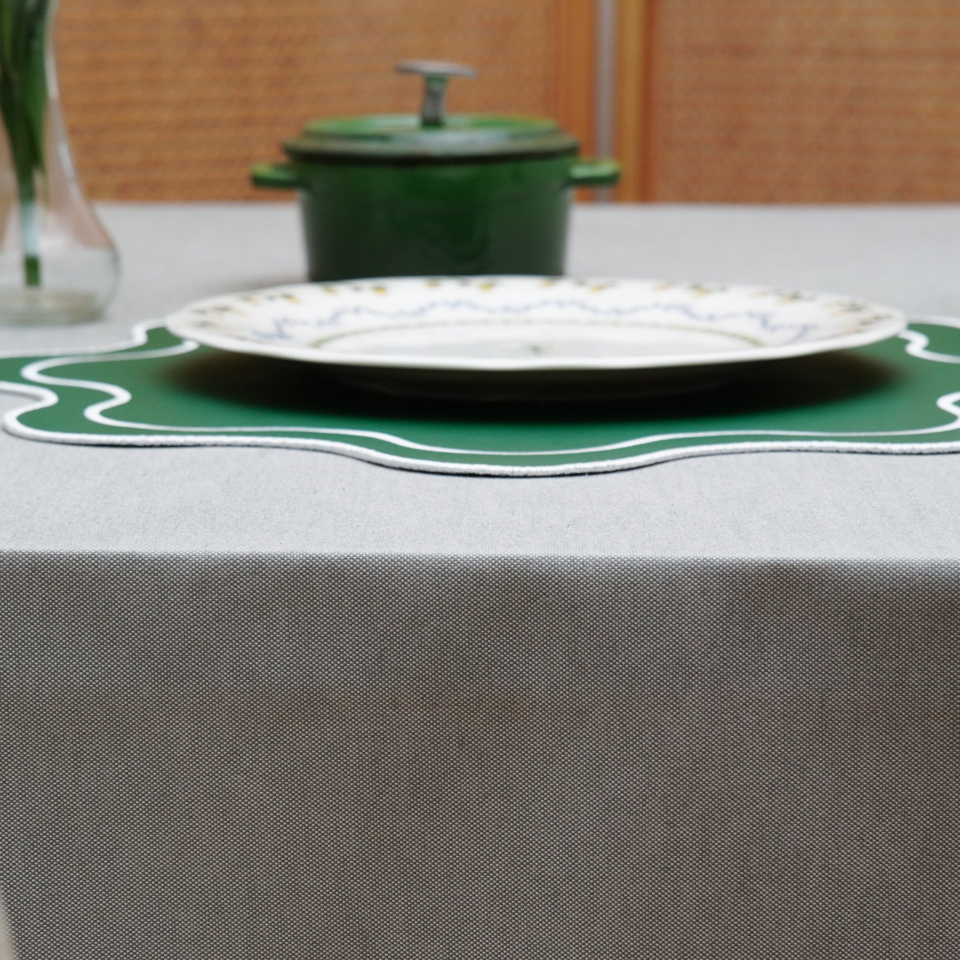 Gray rectangular tablecloth styled with a green placemat and dinnerware for a modern, elegant table setting