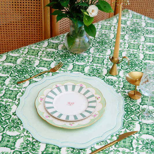 Green and white damask tablecloth styled with plates, gold flatware, candleholder, and a flower vase for an elegant tablescape