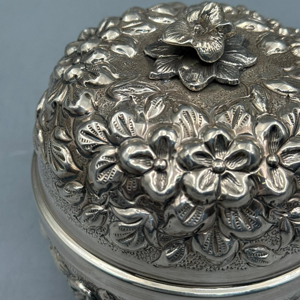 Extreme close-up of the deep-relief floral engravings and textured silver background on the handcrafted 900 silver bonbonniere.