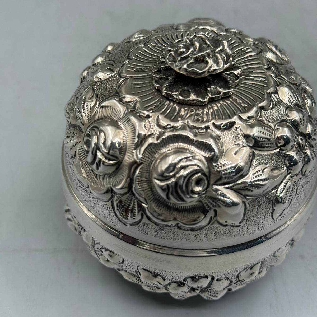 Extreme close-up of the meticulous hand-chased rose relief and textured silver background on the handcrafted bonbonniere lid.