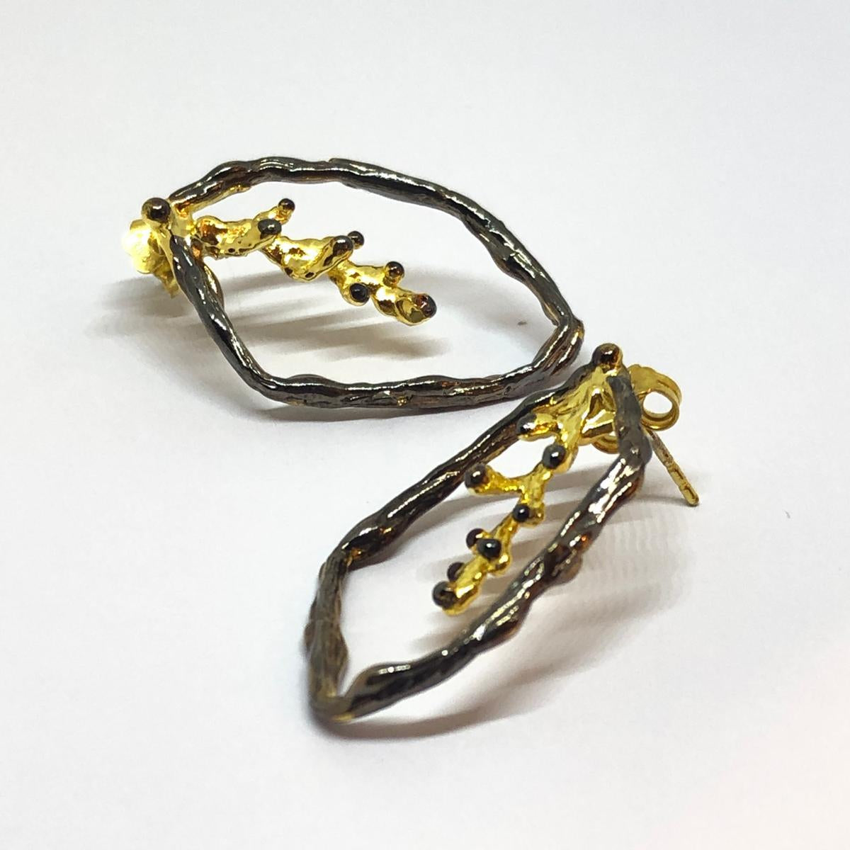 Artisan-made woodland jewelry showing a pair of botanical hoop earrings cast from real pine branches. The dark and gold mixed metals create a stunning visual contrast.