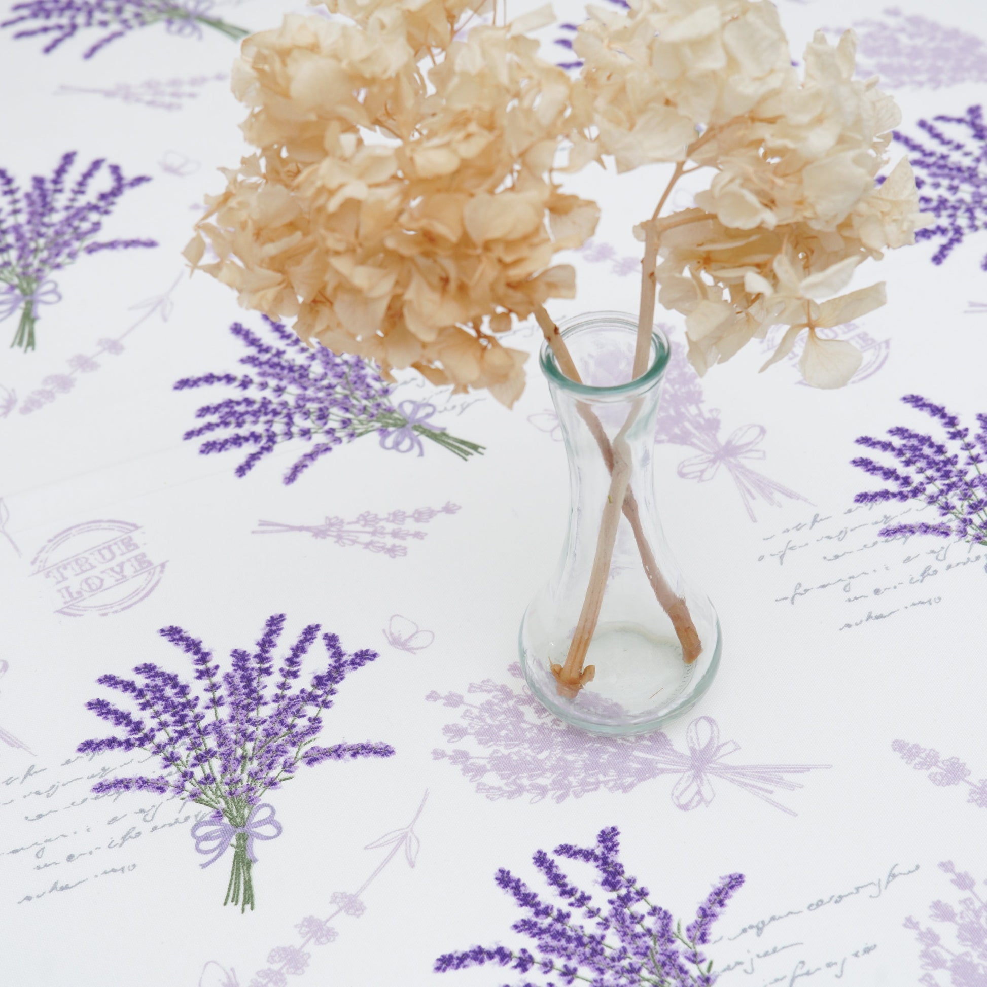 Lavender print rectangular tablecloth with a clear glass vase centerpiece on a bright, minimal table setting