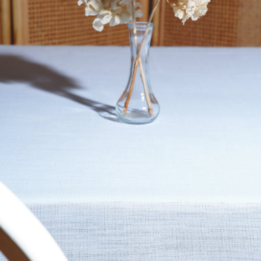 Light blue rectangular tablecloth with a clear glass vase and dried white hydrangeas in soft sunlight.