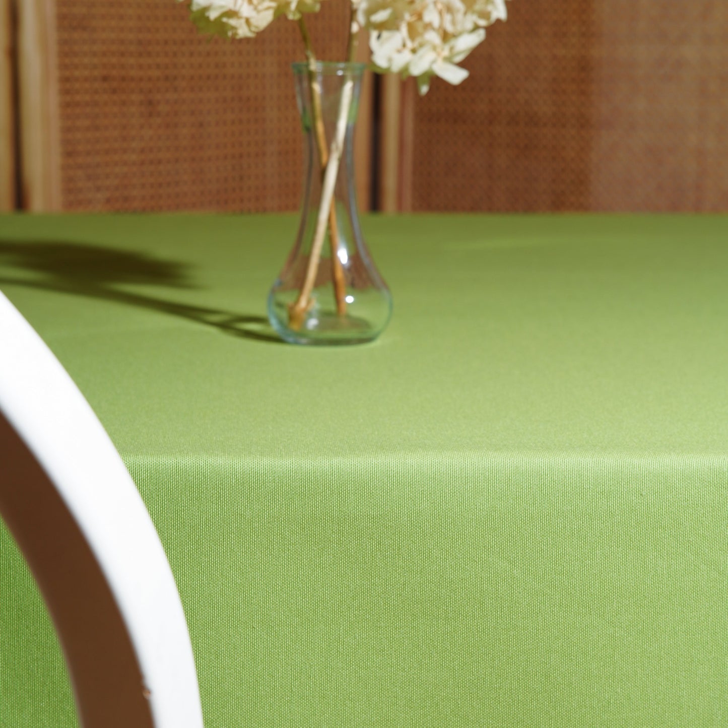 Light green rectangular tablecloth styled with a clear glass vase and dried hydrangeas in warm natural light