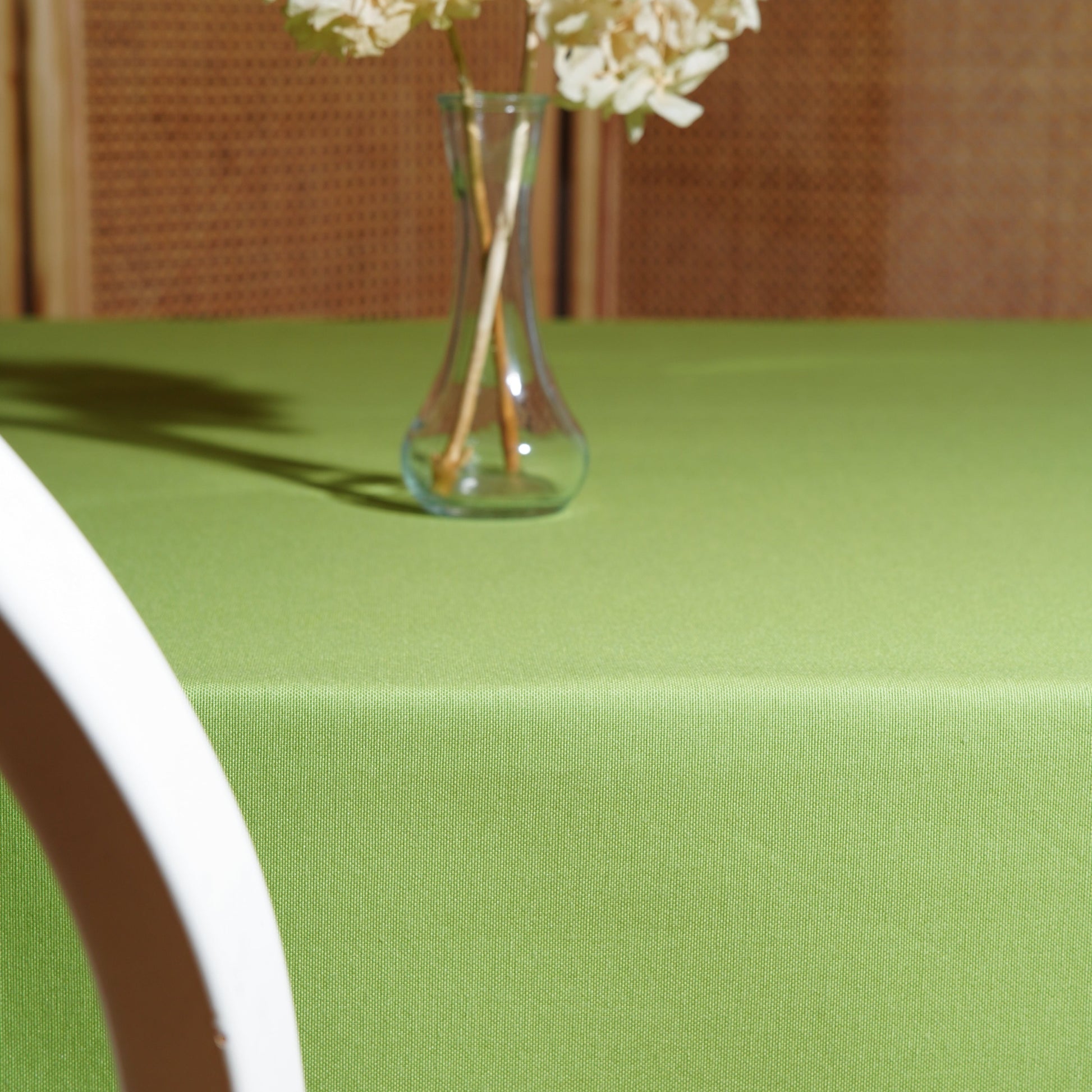 Light green rectangular tablecloth styled with a clear glass vase and dried hydrangeas in warm natural light