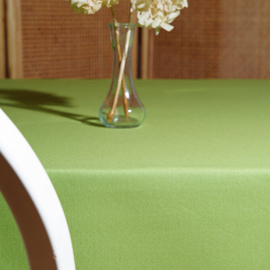 Light green rectangular tablecloth styled with a clear glass vase and dried hydrangeas in warm natural light