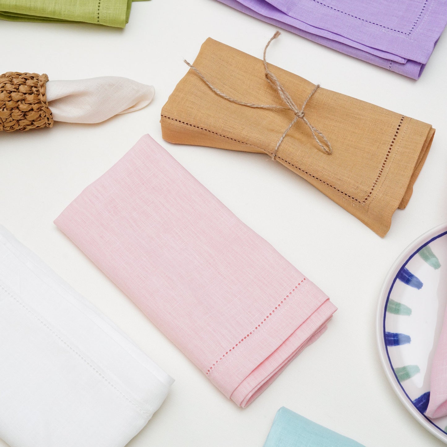 A modern classic dining table arrangement showcasing a cascading pink linen napkin tucked between layered white plates on an embroidered pink placemat.