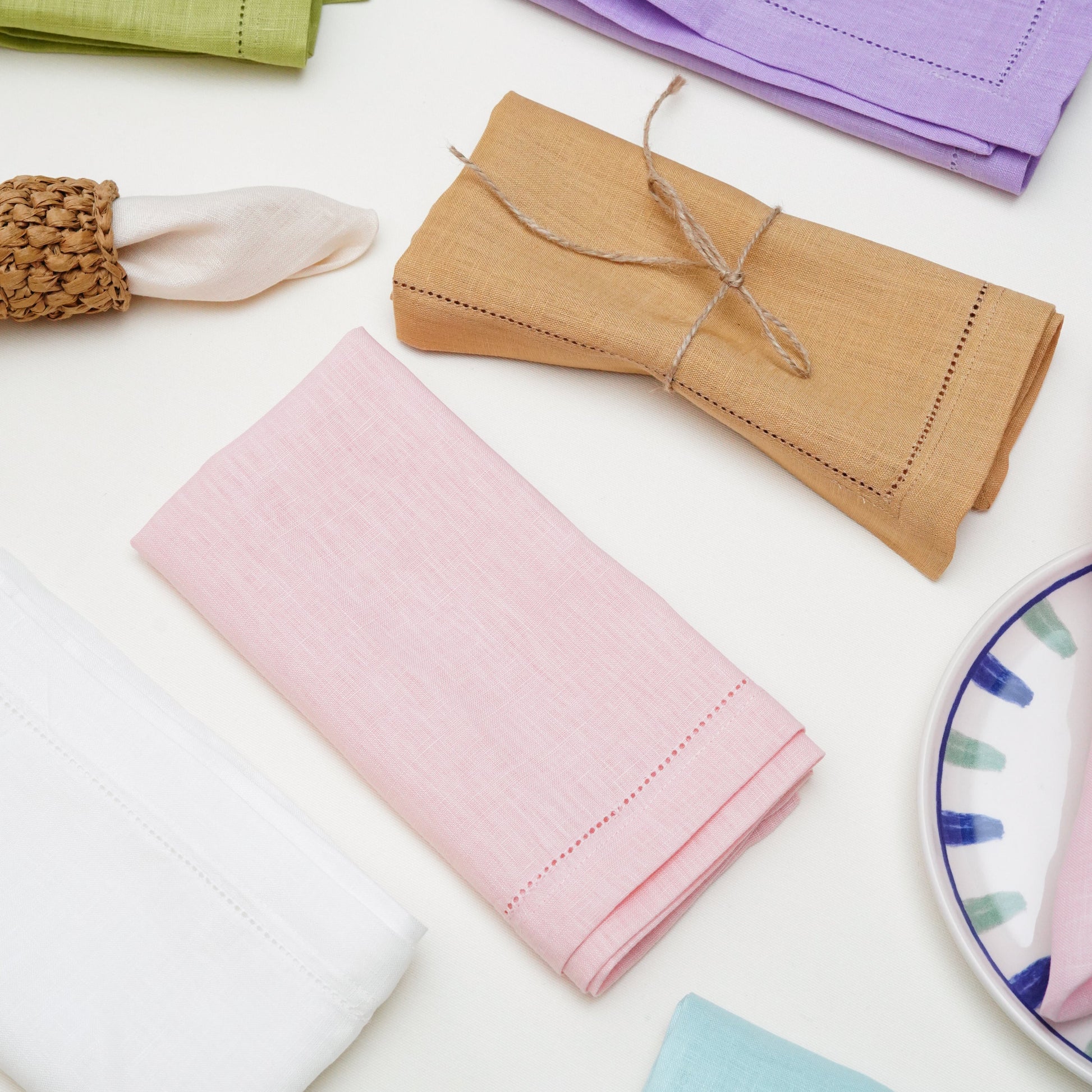 A modern classic dining table arrangement showcasing a cascading pink linen napkin tucked between layered white plates on an embroidered pink placemat.