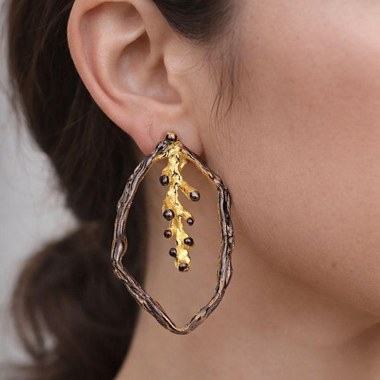 Lifestyle focus on unique two-tone botanical jewelry. The handmade silver and gold pine twig earrings present a beautiful, nature-inspired rustic elegance.
