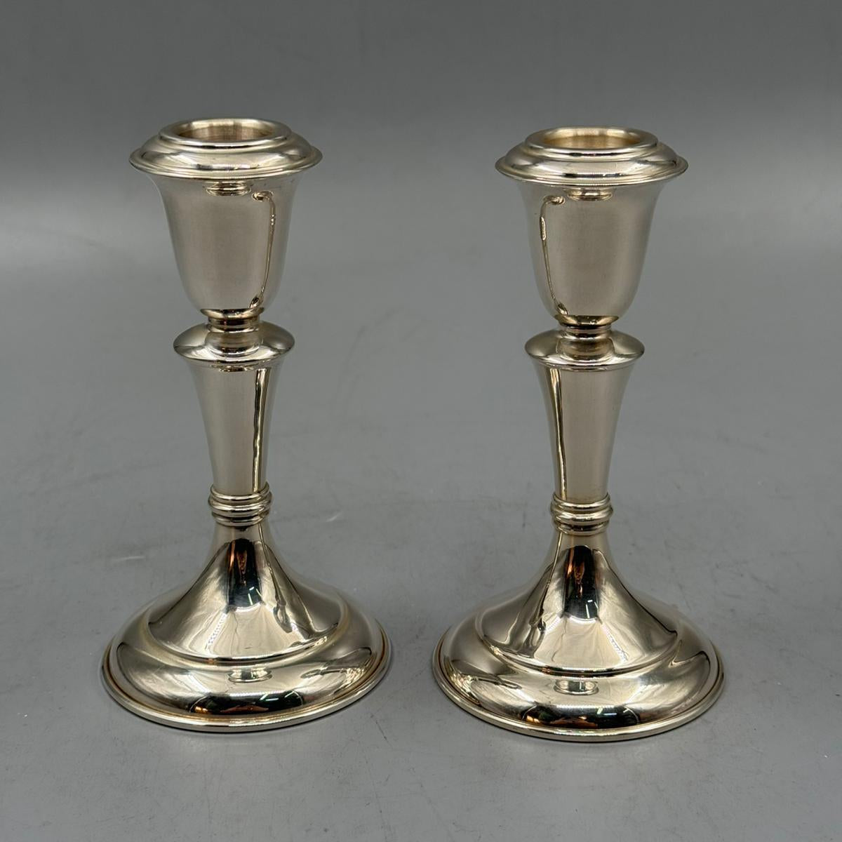 Pair of classic silver candle holders with polished reflective surface and flared tops.