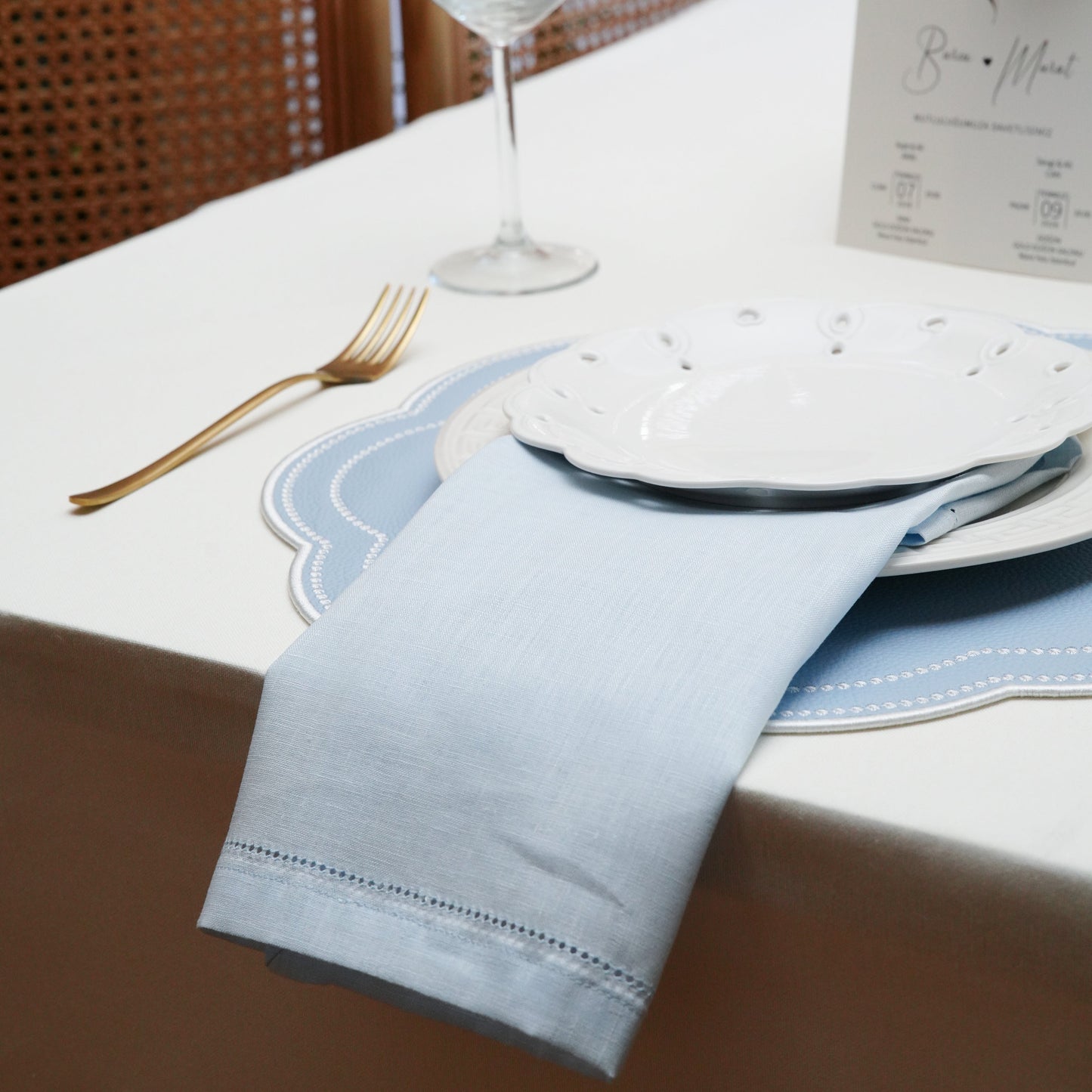 A detailed view of a personalized linen napkin with a sophisticated wreath and initial embroidery, set in a formal dining table arrangement with a navy velvet cloth and elegant place setting.