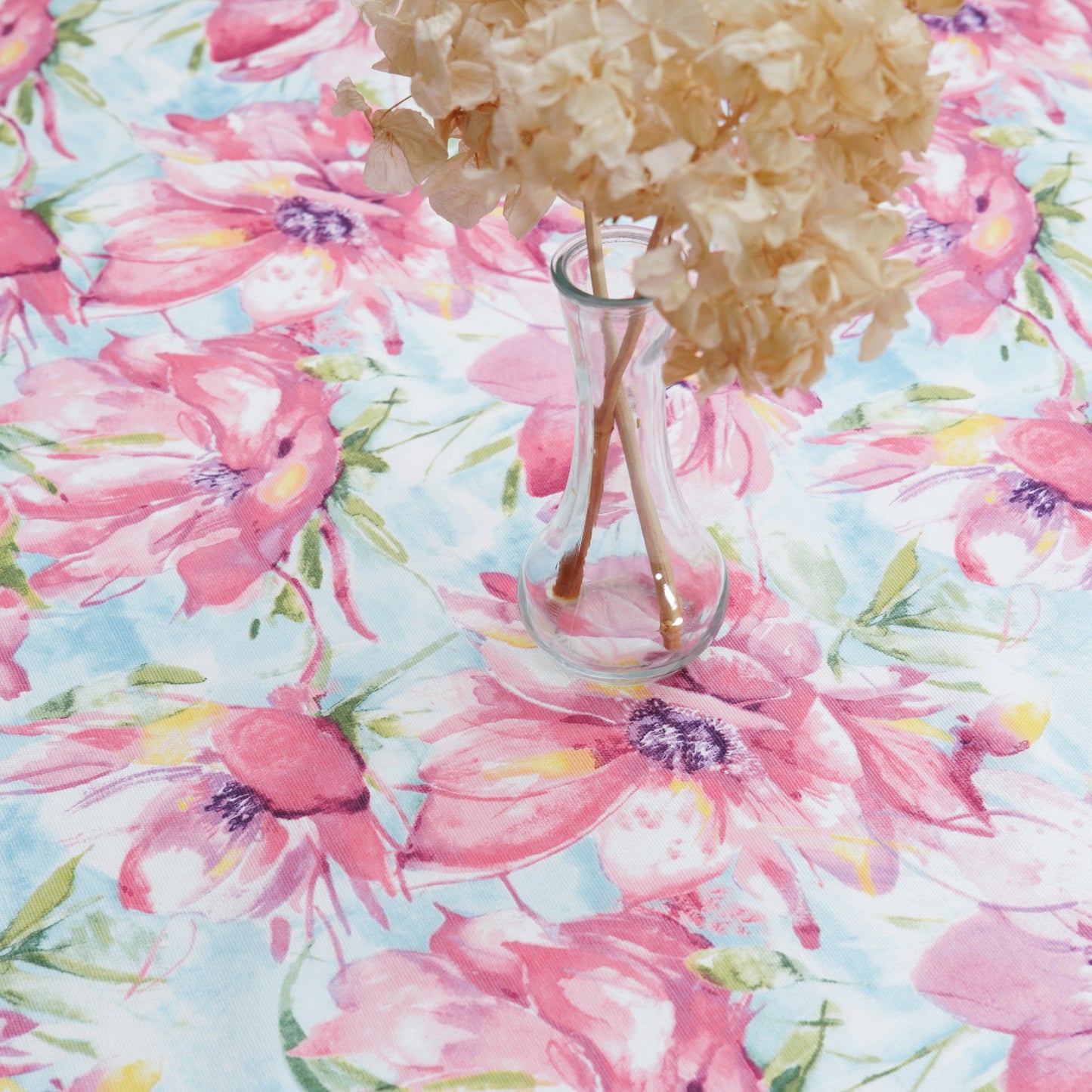 Pink watercolor floral tablecloth with a clear glass vase centerpiece on a bright, airy table setting