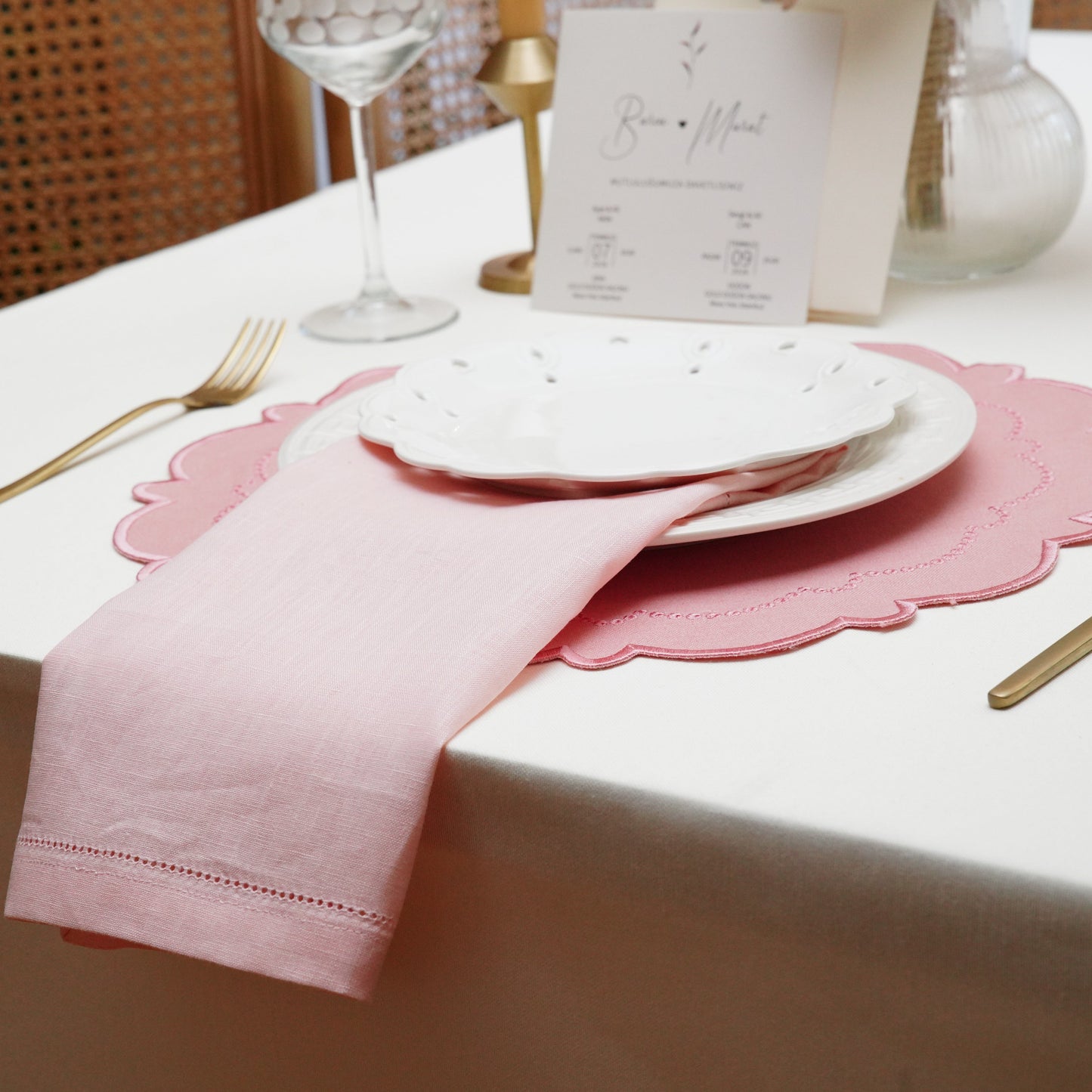 Close-up of a premium quality pink linen cloth napkin highlighting the delicate hemstitch border detail, cascading elegantly off the table edge.