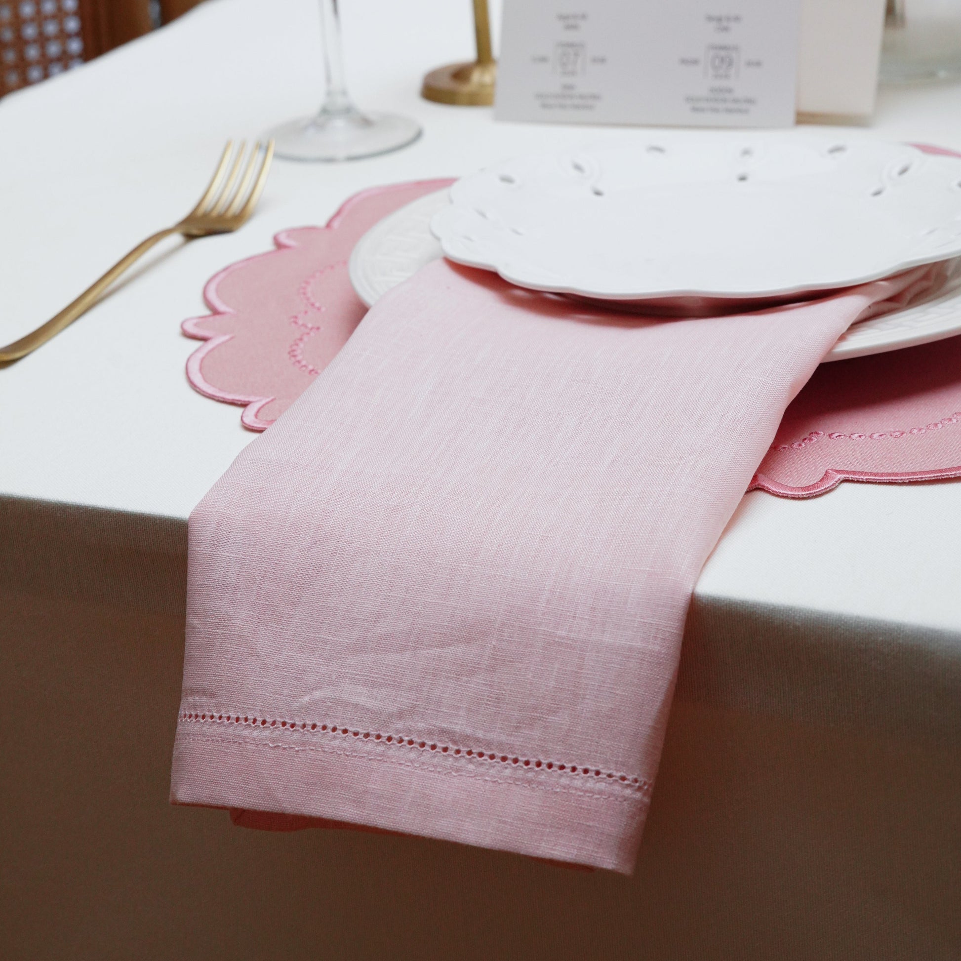 Romantic wedding table setting featuring a rose pink hemstitch napkin and scalloped placemat, creating a soft and elegant dining experience.