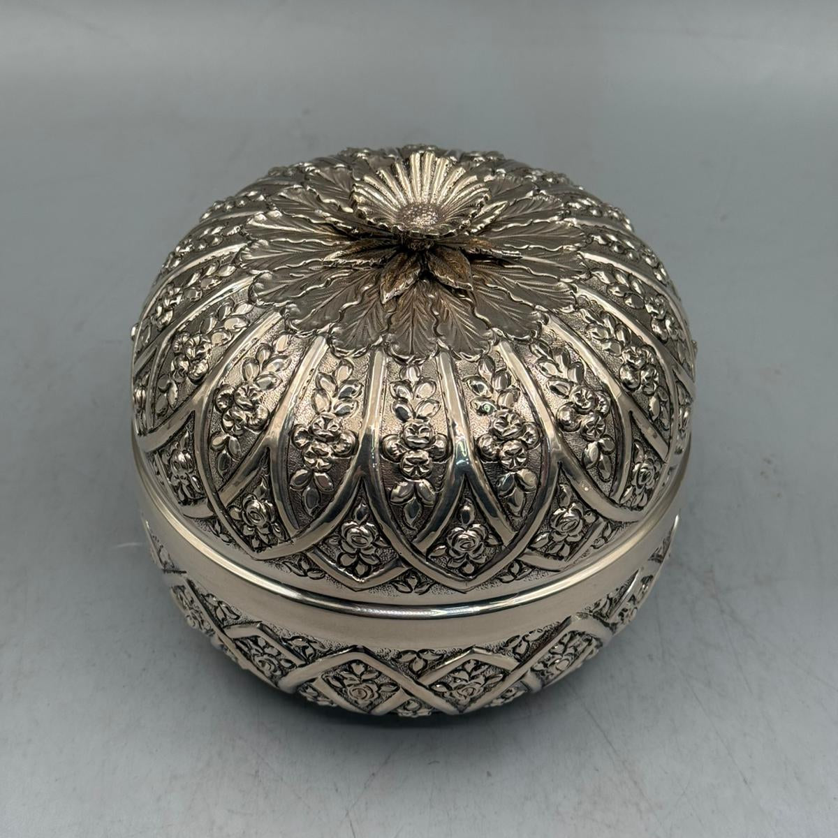 Top-down perspective showing the sculpted flower finial and the radial rose engraving patterns on the sterling silver lid.