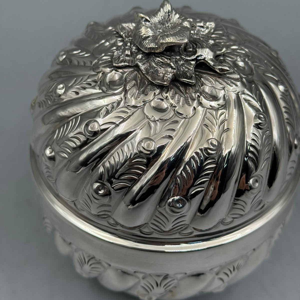 Top-down perspective of the sculpted silver flower handle and radial engraved patterns on the sterling silver lid.