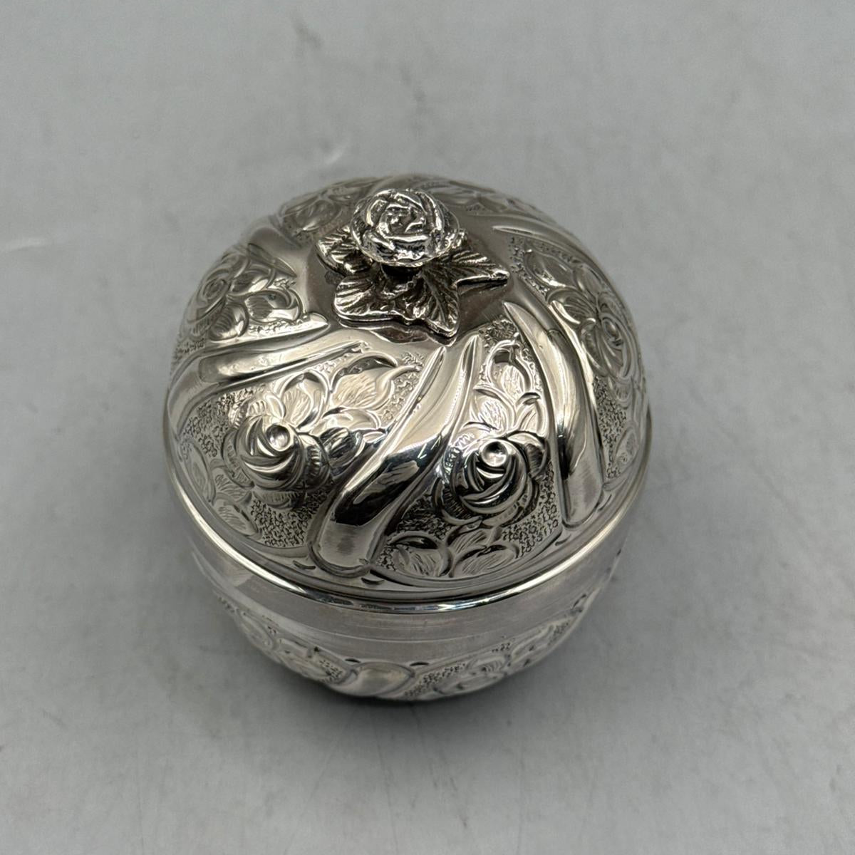 Close-up of the exquisitely sculpted silver rose bud handle and the radial floral engravings on the sterling silver lid.