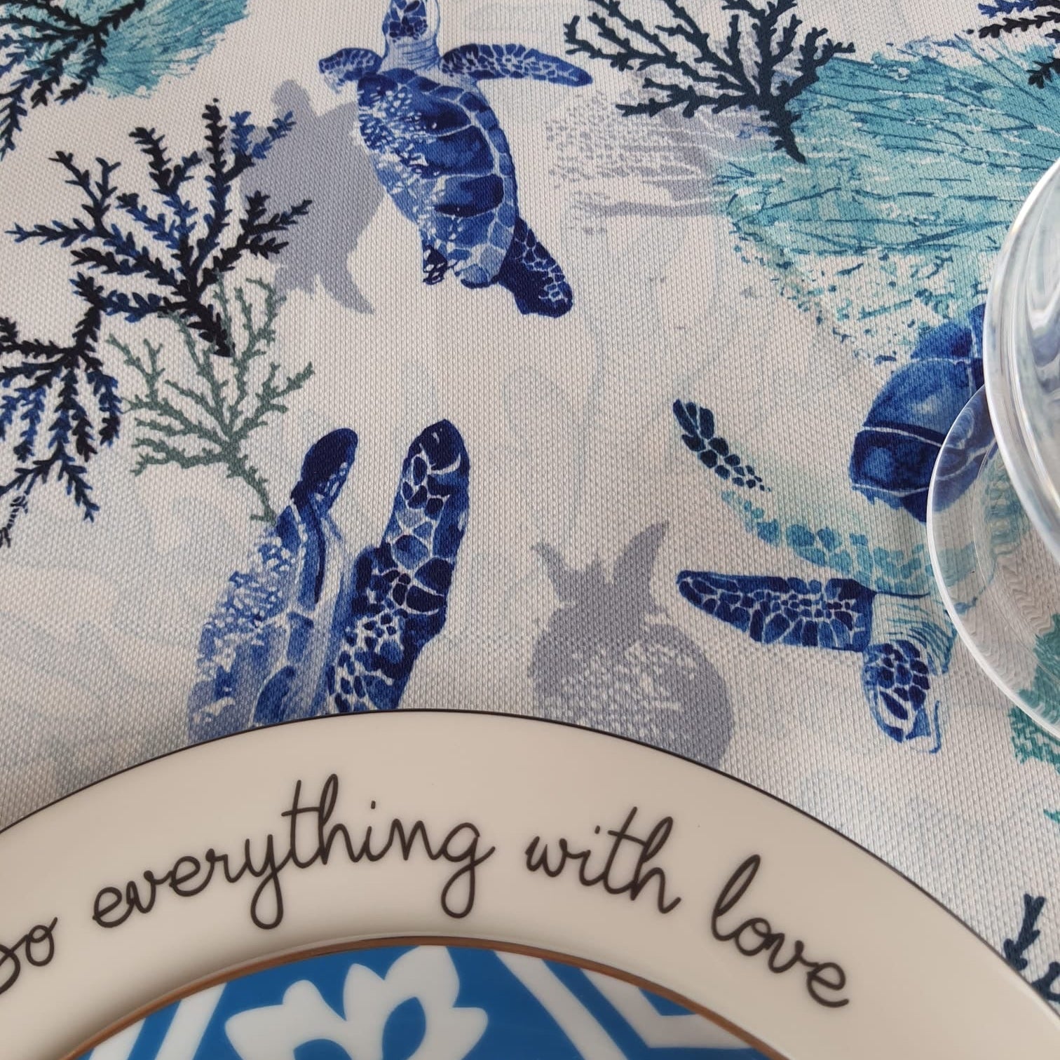 Sea turtle and coral print tablecloth in blue tones styled with a plate and glass for a coastal table setting