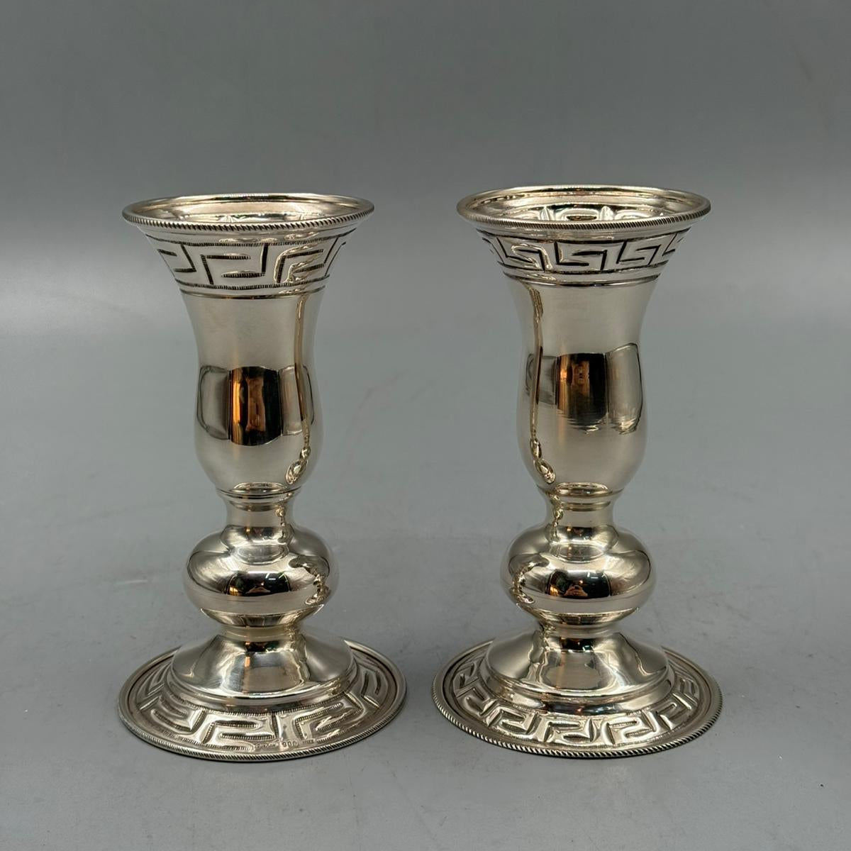 Close-up of a silver candle holder with detailed Greek key design around the rim and base