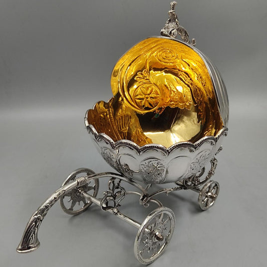 Close-up of a decorative silver carriage bowl with intricate wheel design and golden interior.